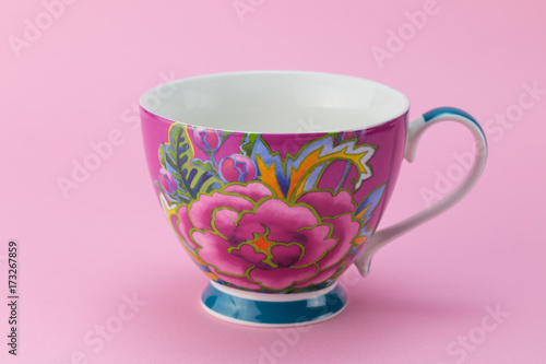 Side view of empty tea or coffee cup with pink and purple flower decoration isolated on pink background