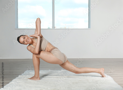 Young beautiful woman doing yoga pose in room with window photo