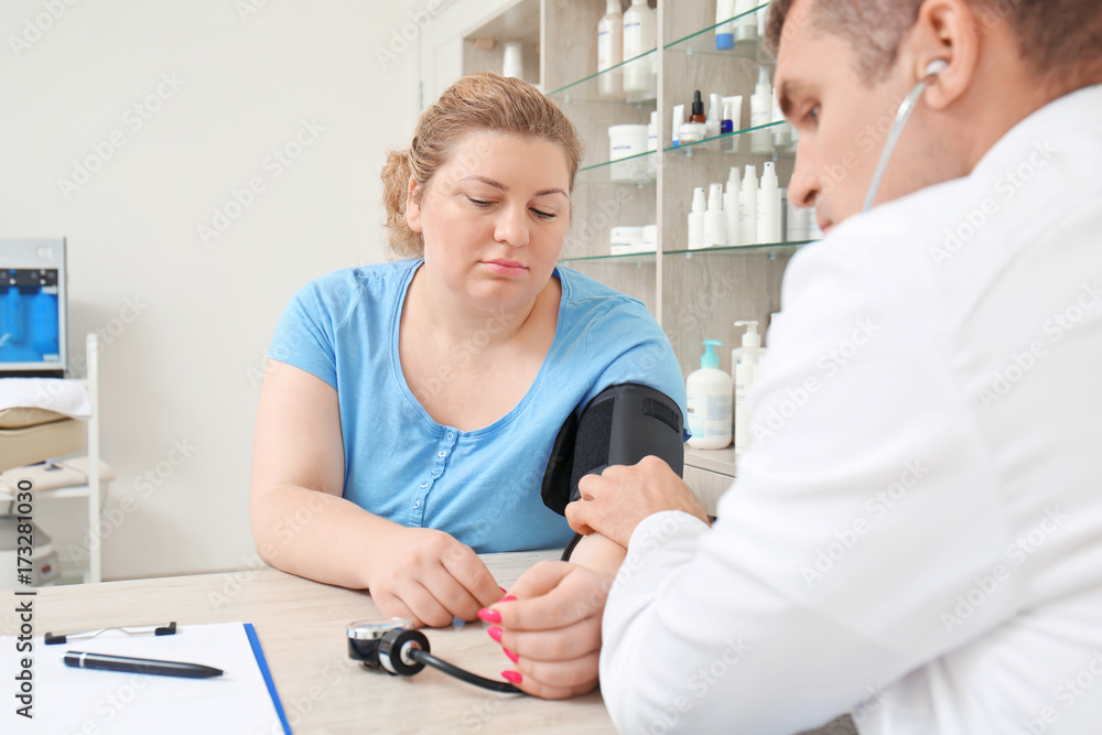 Fototapeta premium Doctor measuring blood pressure of overweight woman in hospital