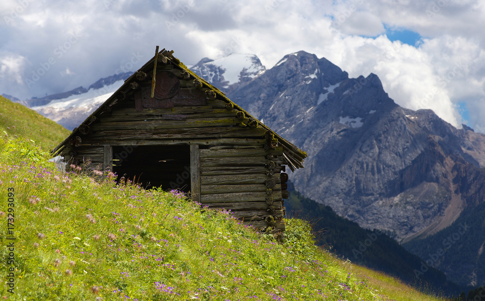 Old cabin in Dolomites with Marmolada peak on the background, Italy