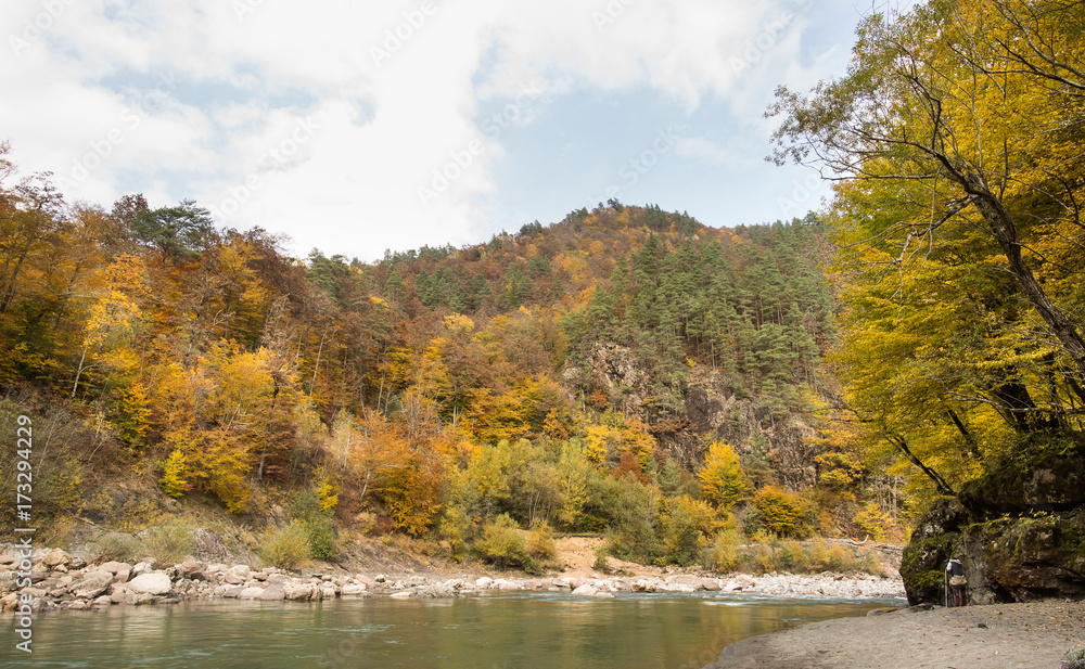 silent, perfection of nature, season concept. at the foot of rocky hills with autumn forests of fire colour there is stony bank and calm river with lazy green waters silent, perfection of nature, season concept. at the foot of rocky hills with autumn forests of fire colour there is stony bank and calm river with lazy green waters