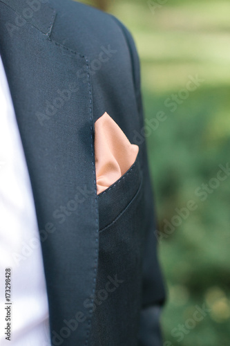 fashion, celebrating, dressmaking concept. in left lapel of exquisite black costume for young fiance there is simple but stylish elemet, it is small peachy handkerchief