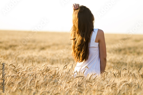 womanhood, beauty, travelling concept. in bright light of rising sun there is darkhaired woman in dazzling white dress standing among high stems of some cereal culture