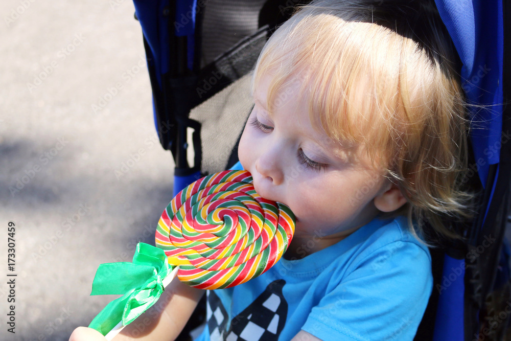 Toddler eating a yummy colorful lollipop. Baby boy with swirl lollipop
