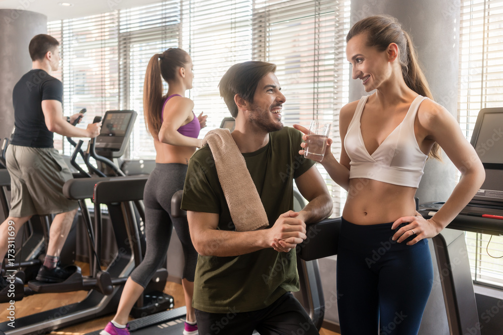 Fototapeta premium Cheerful young man and woman chatting while having break from running exercise in modern gym 