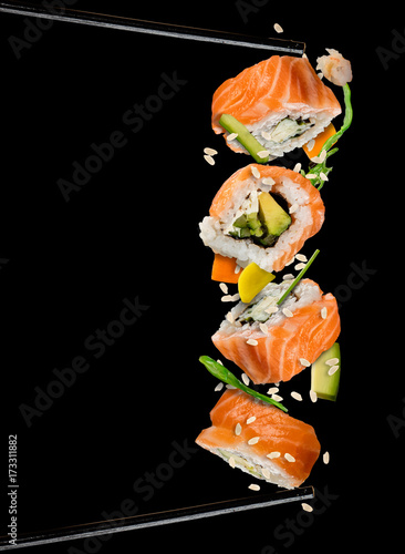 Sushi pieces placed between chopsticks on black background