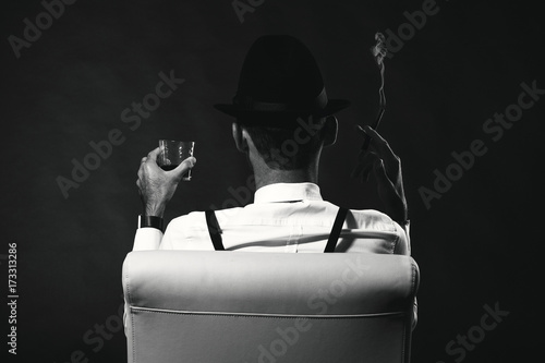 Autocolant an unidentified man in a suit and hat with a cigar and whiskey staring into the distance