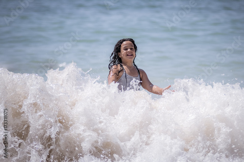 Niña morena bañándose en el mar y jugando con las olas. © Trepalio