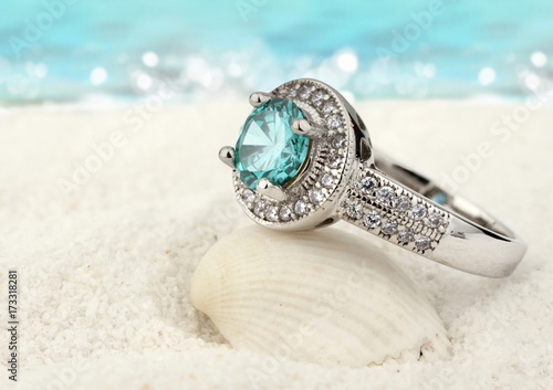 Jewelry ring with clean aquamarine gem on sand beach background
