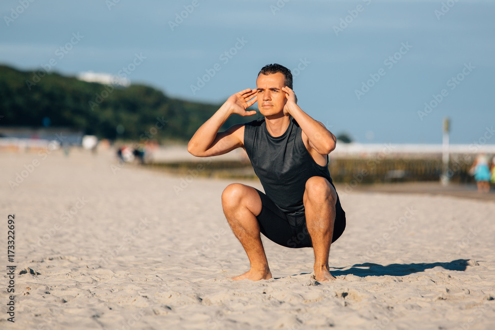 Handsome young man doing sit-ups on the beach sea. Sportsman doing workout outdoors. Healthy lifestyle concept