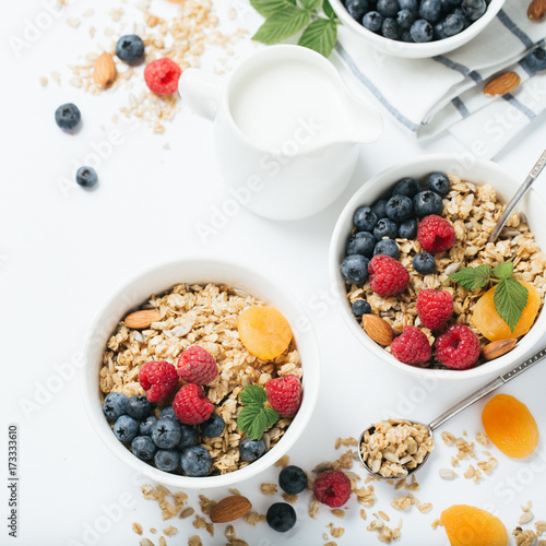 Homemade granola and healthy breakfast ingredients - milk, dried fruit and berries on white background