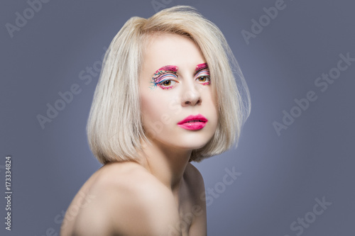 Beauty and fashion Ideas. Portrait of Caucasian Blond Female With Vivid Artistic Facial Makeup Against Gray.