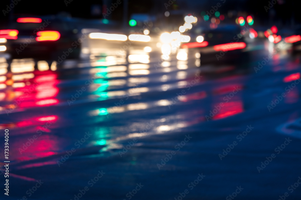 blurry image of cars driving on wet road in the city with headlights switched on