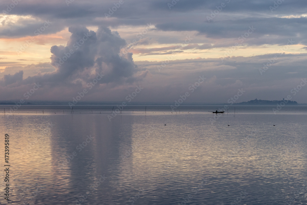 A lake at dusk, with beautiful clouds reflections and a distant fisherman on a little boat