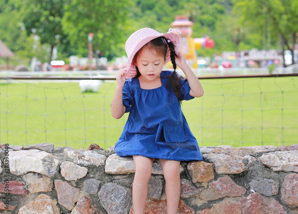 Cute little asian girl wear straw hat sitting on the stone wall against