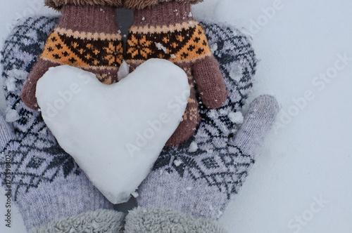 female hands in mittens and baby hands in mittens keep the heart out of the snow against the background of white snow