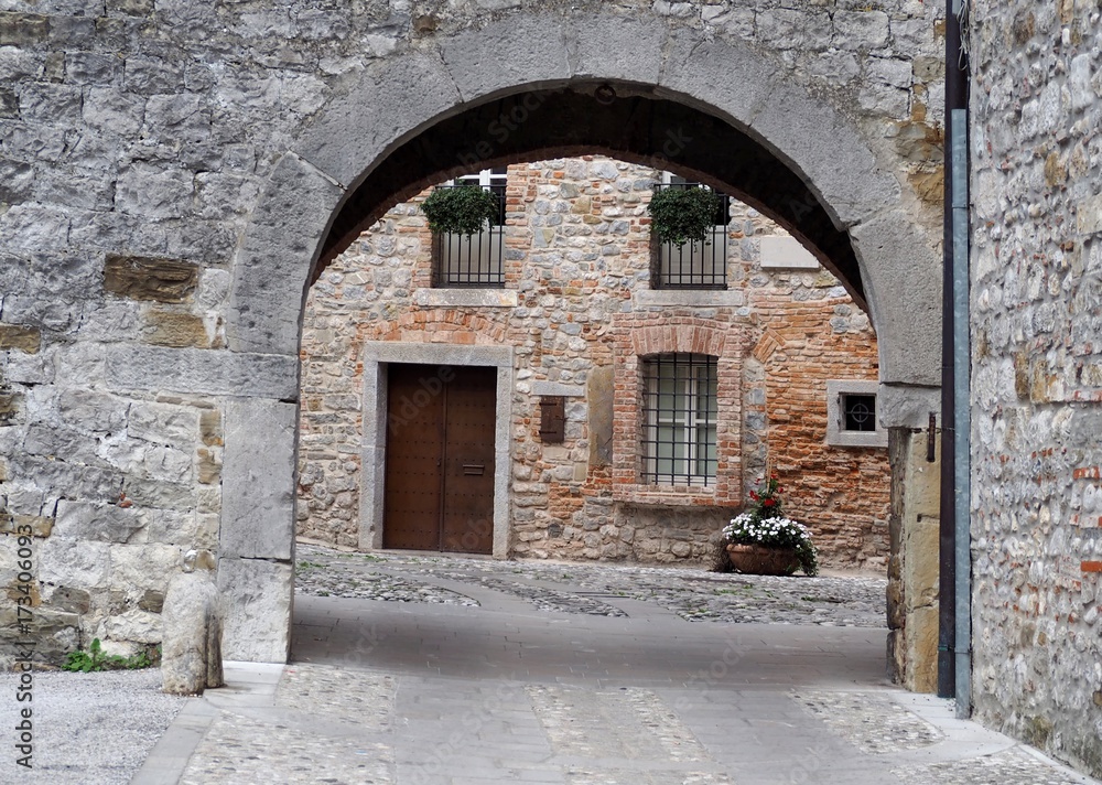 Medieval urban background. A stone arch, a stone street and an ancient brick wall house facade in the town of Cividale