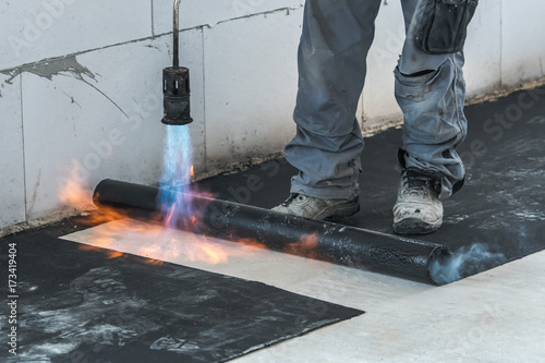 Professional installation of the waterproofing on the concrete foundation. Installation with rolls of bituminous sealing membrane by heating and melting of bitumen rolls by torch to flame while sealin