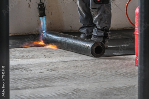 Professional installation of the waterproofing on the concrete foundation. Installation with rolls of bituminous sealing membrane by heating and melting of bitumen rolls by torch to flame while sealin photo