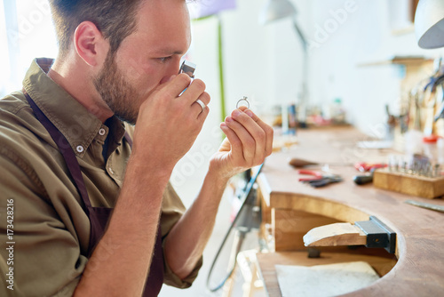 Side view portrait of jeweler inspecting ring through magnifying glass in workshop