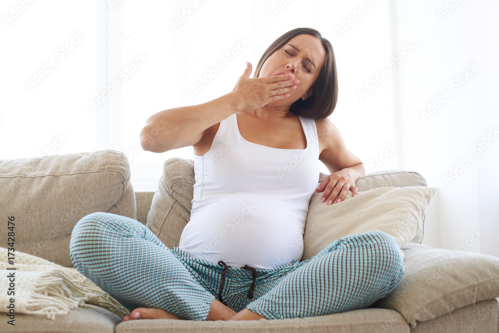 Tired pregnant woman yawning while sitting on sofa Tired pregnant woman yawning while sitting on sofa