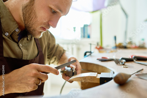 Photography Side view portrait of young jeweler making golden ring in workshop, forming and