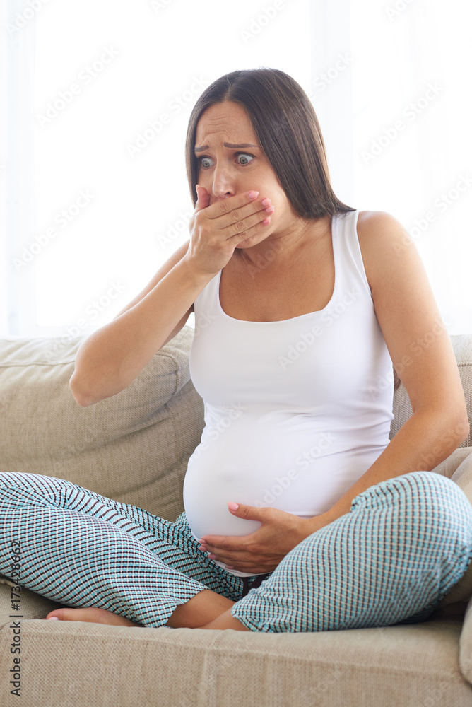 Pregnant young woman sitting on sofa and feeling sick Pregnant young woman sitting on sofa and feeling sick