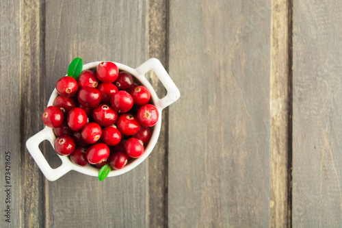 Fresh cranberry in white ceramic bowl on wooden background