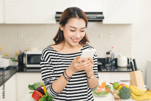 Smiling asian woman in the kitchen writing text message