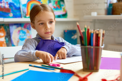 Portrait of adorable little girl in pre-school, daydreaming during lesson in art class