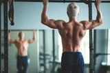 Muscular athlete man making Pull-up in gym. Bodybuilder training in fitness club showing his perfect back and shoulder muscles. Toned image