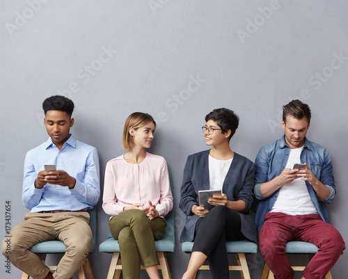 Busy business people, wait for meeting with boss: two guys chattes over cell phone or surf social networks and women have pleasant conversation, make acquintance, find common topic to discuss photo