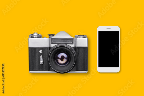 Retro camera and contemporary smart phone lies on yellow surface. Modern and retro supplies. Revolution concept. Photographer`s workplace. Innovative technology concept.