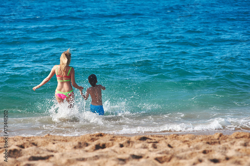 Caucasian mom and son running into the sea water. Back view. © Artem