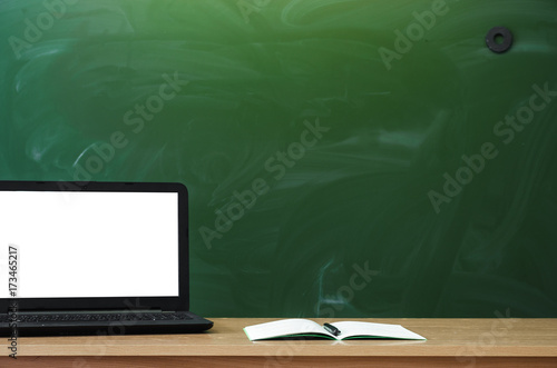 Teacher or student desk table on school blackboard background. Education background. Mockup education concept. Laptop with blank screen and copy book on the table.