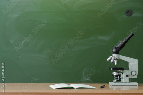 Teacher or student desk table. Education background. Education concept. Microscope and notebook on the table on blackboard (chalkboard) background. Chemistry or biology lesson.