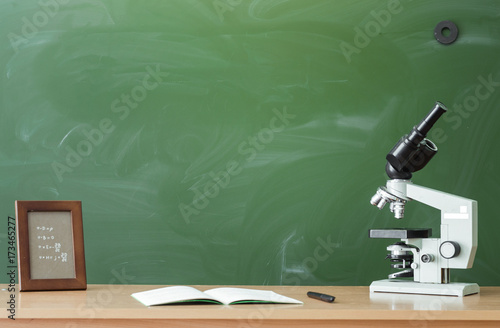 Teacher or student desk table. Education background. Education concept. Copybook, pen, microscope and photo frame on the table on blackboard (chalkboard). Chemistry or biology lesson.