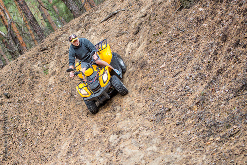 Man riding an ATV quadbike over rough terrain in a beautiful autumn pine forest with carpet of fallen needles