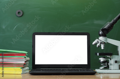 Teacher or student desk table. Education background. Education concept. Laptop with blank screen, microscope and stacked books on the table.