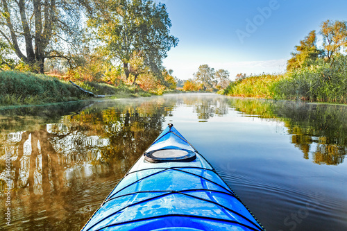 View from the blue kayak on the river banks with autumnal yellow leaves trees in fall season. The Seversky Donets river, autumn kayaking. View over nose of bright blue kayak. photo