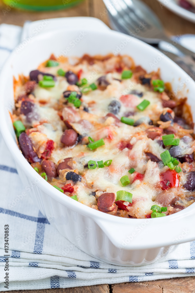 Baked rice casserole with different kinds of beans, cheese and paprika, in white ceramic baking dish, vertical Baked rice casserole with different kinds of beans, cheese and paprika, in white ceramic baking dish, vertical