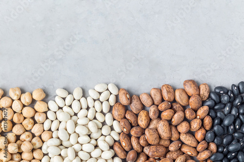 Different kinds of beans: black, pinto, white and chickpeas, on a concrete background, copy space, horizontal