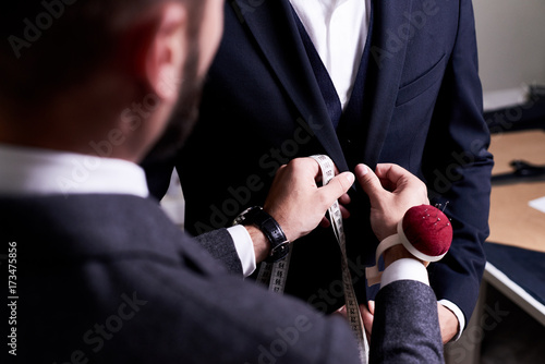 Over shoulder view of bearded fashion designer fitting bespoke suit to model, close-up shot photo
