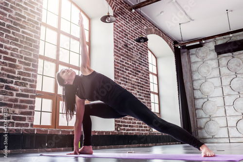 Young sporty woman practicing yoga doing triangle pose, trikonasana, on mat