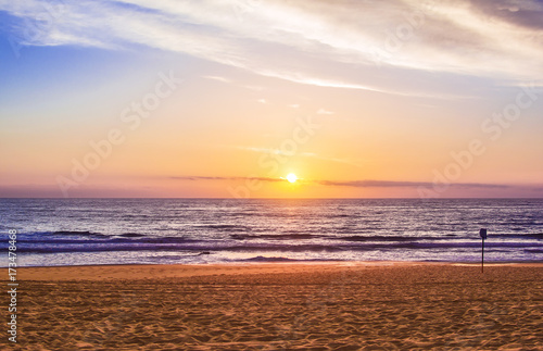 The setting sun beautifully illuminates the calm ocean and beach
