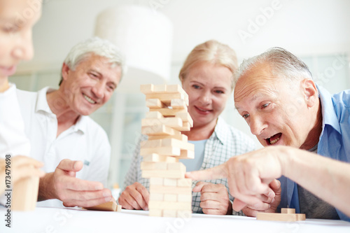 Group of old friends playing jenga and building structure from wooden blocks on table