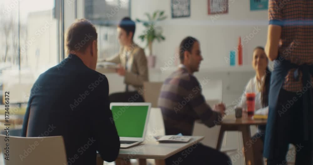 A man sitting in a cafe uses a laptop with a green screen. Around the people. The waiter is in the frame. Shot on RED Epic Camera. A man sitting in a cafe uses a laptop with a green screen. Around the people. The waiter is in the frame. Shot on RED Epic Camera.