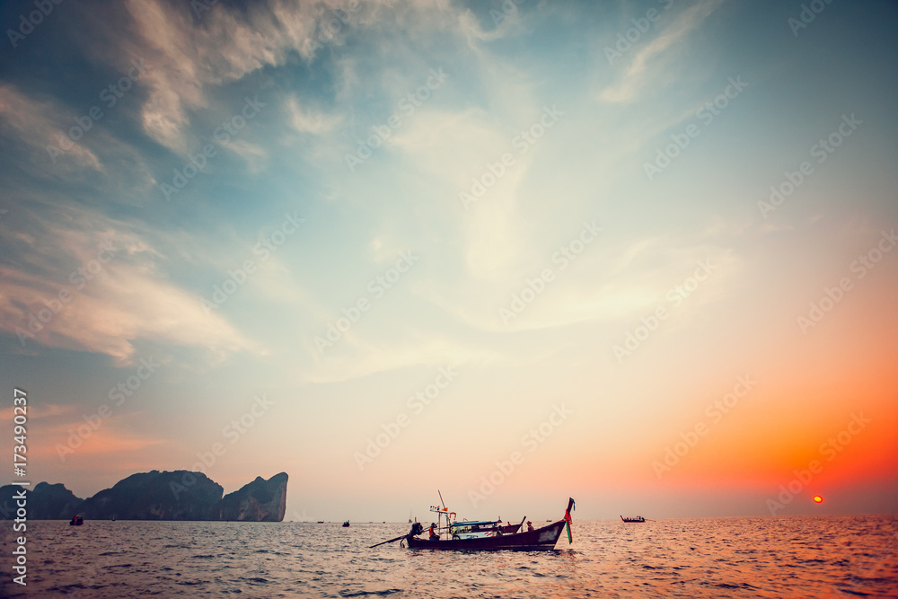 Traditional long boat and beautiful tropical sunset in Krabi, Thailand. Dramatic and picturesque evening scene. Ocean and colorful cloudy sky in the background. Nature landscape. Travel background