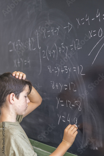 Schoolboy solving a problem on a blackboard.