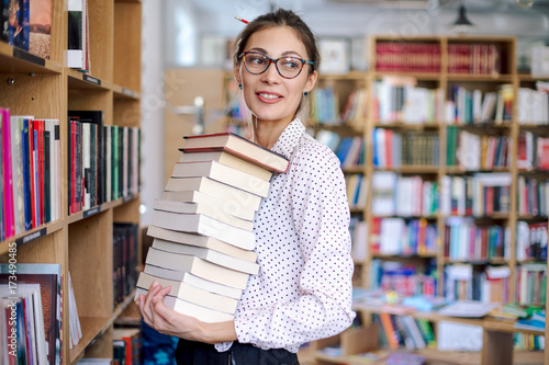 Young woman with a stack of books in library photo